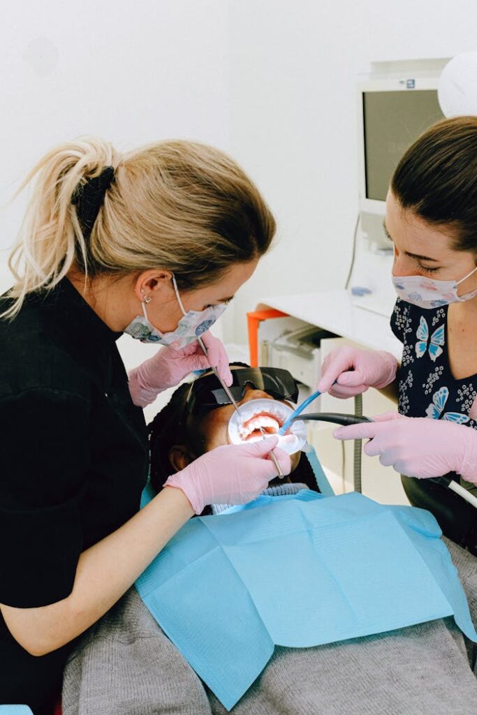 Female dentist with assistant treating teeth of patient in clinic